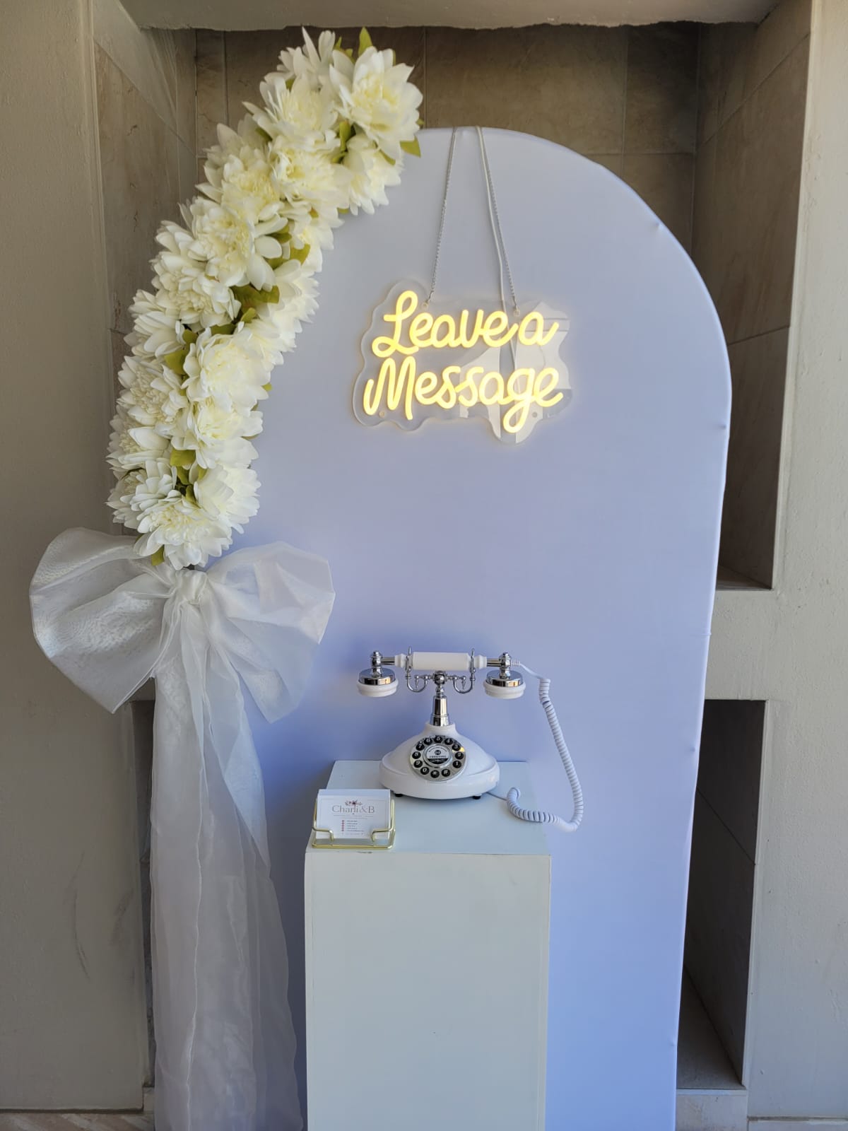 Video guestbook stand with white floral arch and Leave a Message neon sign